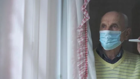 Old man in blue face mask stands at plastic window closeup Stock Footage 134998254