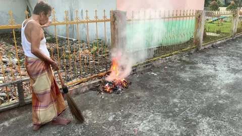 Old man burning trash of fallen leaves on a residential street in the afternoon Stock-Footage 241258170
