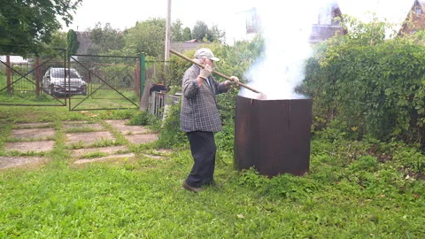 An old man burns branches of shrubs and trees after pruning in a garden stove Stock Footage 137325213