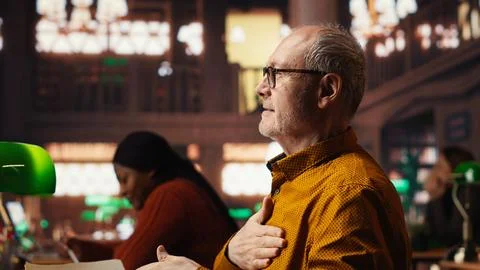 Old man in the campus library struggles with breathing and feeling unwell Stock Photos