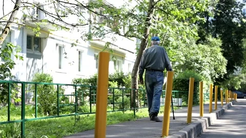 An old man with a cane walks along a city street on a sunny day. Stock Footage 161438655
