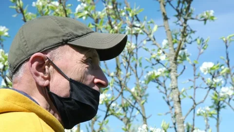 Old man in cap and black mask watches white flowers closeup Video stock 130888234