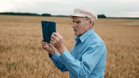 Old man in cap standing at field and using tablet device. Сoncept of modern Video stock 169702082