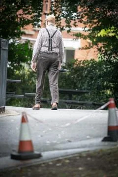 An Old Man Carrying An Umbrella Walking Out Of A Park Stock Photos