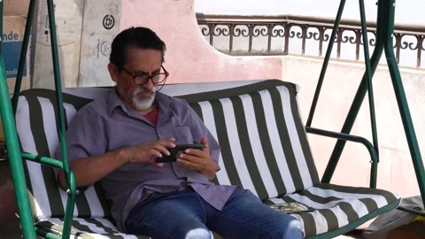 An old man checking his phone in a rocking chair lounging in the daylight Stock Footage 147880869