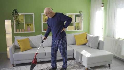 Old man cleaning house gets tired while using vacuum cleaner. Video stock 232235502