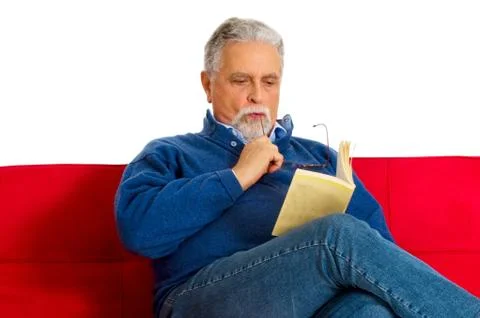 Old man on the couch reading a book Stock Photos