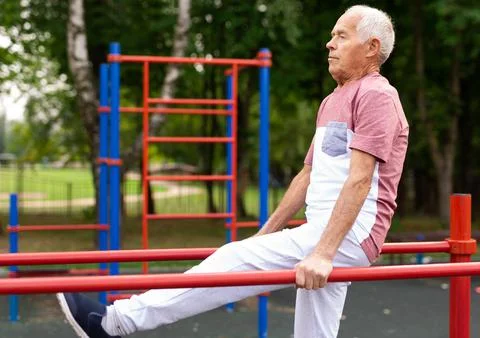 Old man doing exercises on parallel bars outdoors Stock Photos