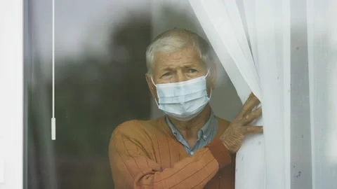 Old man with face mask put the curtain aside, home alone Vidéo 141356353