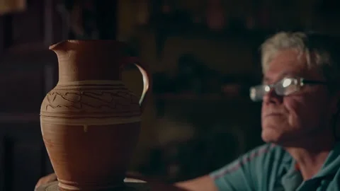 Old man in glasses controls handmade ceramic pot spinning on pottery wheel Stock Footage 264092679