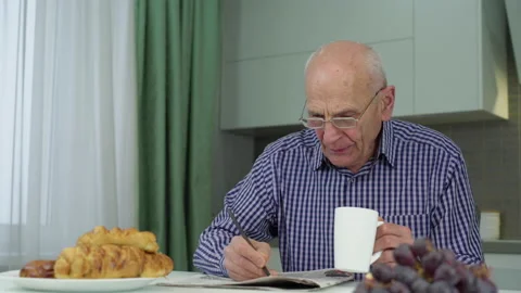 Old man in glasses with cup of tea solves crossword puzzle Video stock 239086435
