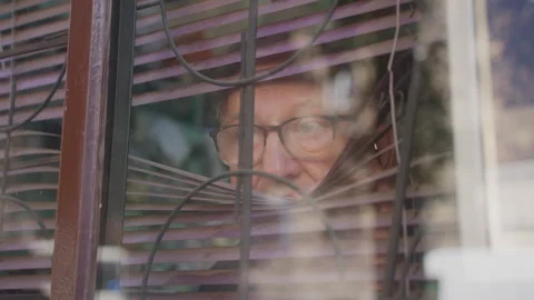 Old man in glasses opens blinds and looks out window, from outside Stock Footage 252865337