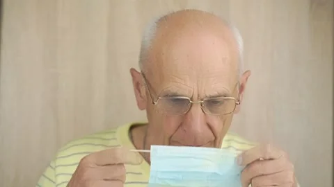 Old man in glasses puts blue disposable mask on at home Stock-Footage 134997812