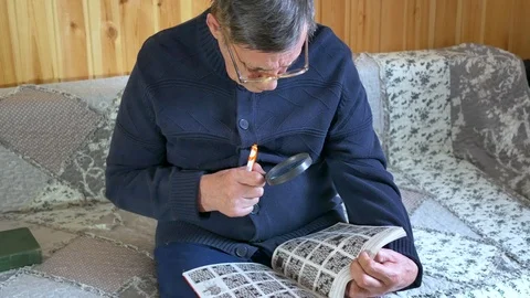 An old man with glasses is sitting on the sofa writing with a pen and using a Stock Footage 111489305