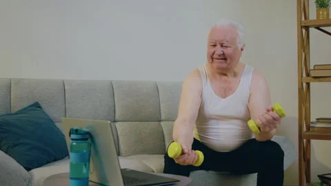 Old man in a good mood doing exercise at home while sitting on the sofa and Stock Footage 255109971