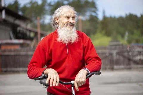 Old man with a gray beard resting on the handlebar of a bicycle Stock Photos