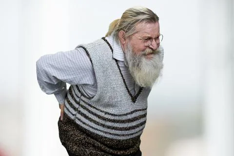 Old man with gray beard suffering from backache on blurred background. Stock Photos
