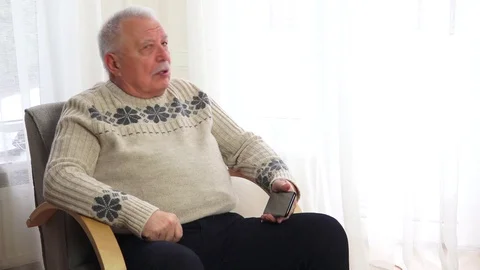 Old man in grey sweater waves goodbye sitting in armchair Stock Footage 109191659