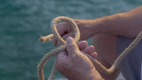 Old man hands tying knot with old rope, sea surface in background 4K Stock Footage 94523475