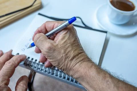 Old man hands writting notes while drinking coffee in living room Stock Photos
