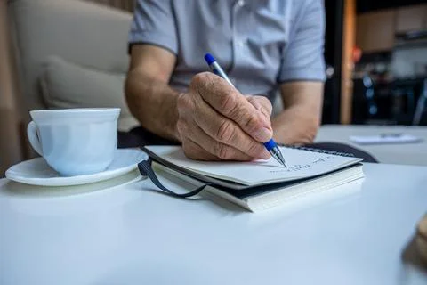 Old man hands writting notes while drinking coffee in living room Stock Photos