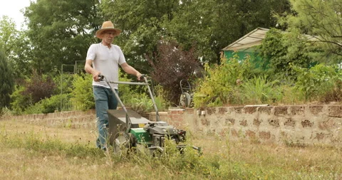 Old man in hat cutting grass in his patio Stock Footage 155738312