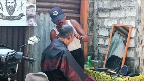 : An old man in a hat is shaving his friend's hair at his barber shop. Stock Footage 303339398