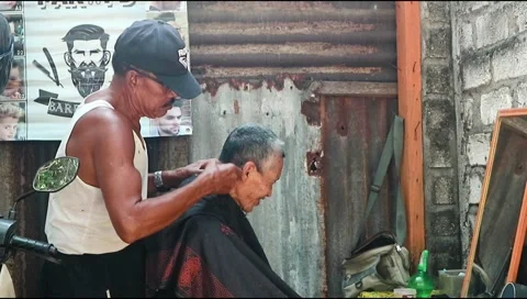 : An old man in a hat is shaving his friend's hair at his barber shop. Stock Footage 303339417