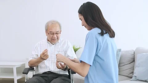Old man holding a pill capsule and a glass of water prepared by caregiver. 動画素材 247350232