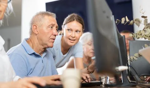Old man learning computer programs with teacher in training room Fotos de archivo