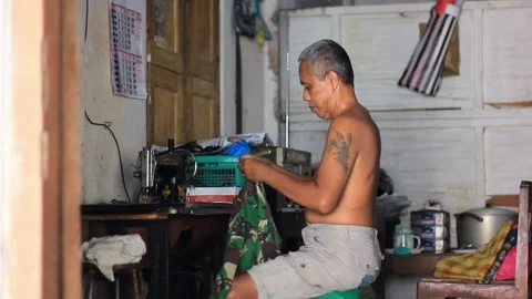 Old man learns to sew torn pants Stock Footage 282065496