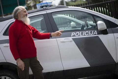 An old man with a long gray beard points a finger at a police car Foto stock