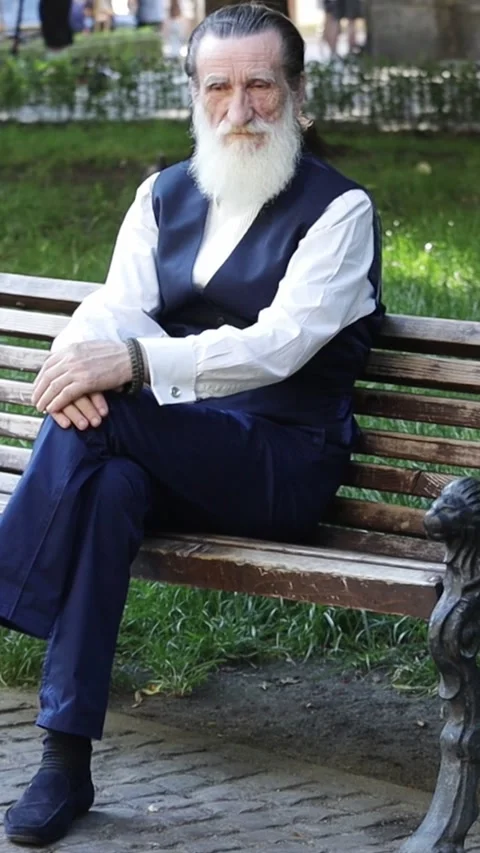 Old man with long white beard sitting on park bench with thoughtful expression Stock Footage 312188577