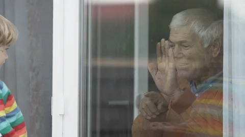 Old man look out window, grandchild outside raises hands to touch grandparent Stock Footage 141357012