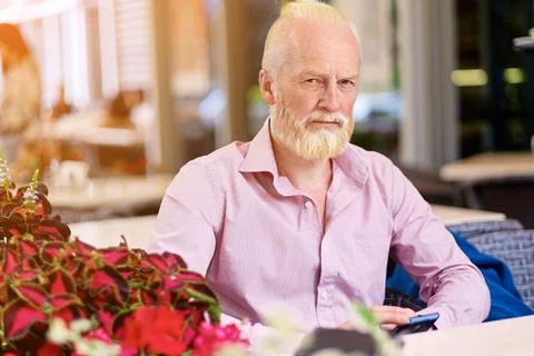 Old man looking at camera sitting at table in cafe 库存照片