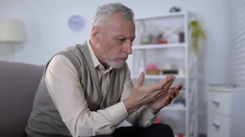 Old man looking at hand trembling, distressed by tremor, early Alzheimer symptom Video stock 108135803