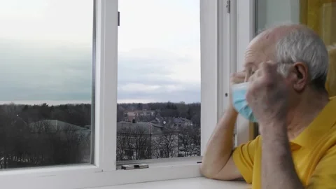Old man looks at the camera then out the window and takes off the medical mask Stock Footage 155961712