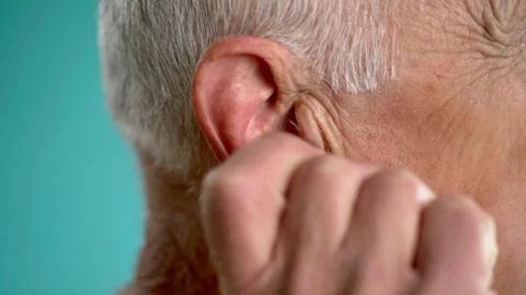 Old man massaging earlobe while standing on blue background Stock Footage 274304584