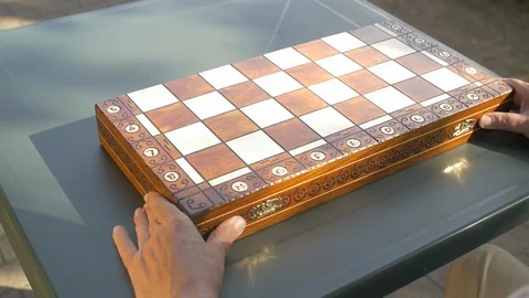 Old man opens the chess game box outside in the garden on the table and puts the Stock Footage 118536052