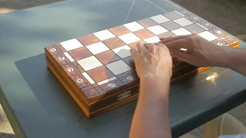 Old man opens the chess game box outside in the garden on the table and puts the Stock Footage 118538550