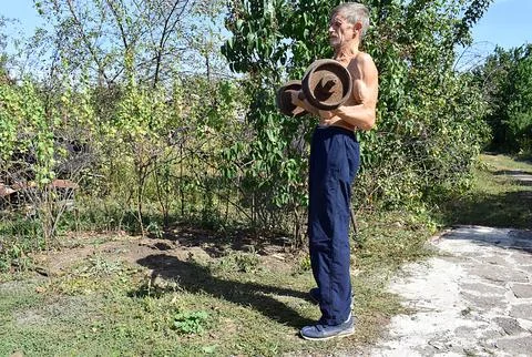 An old man performs exercises with a barbell. Stock Photos
