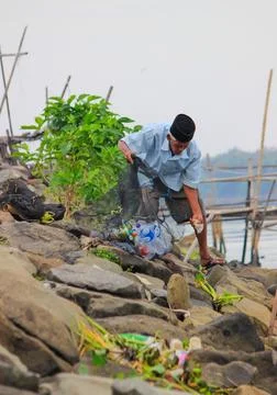 An old man is picking up plastic waste by the river Stock Photos