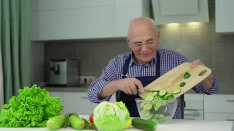 Old man pours cut cucumber into bowl from cutting board Stock Footage 239084963