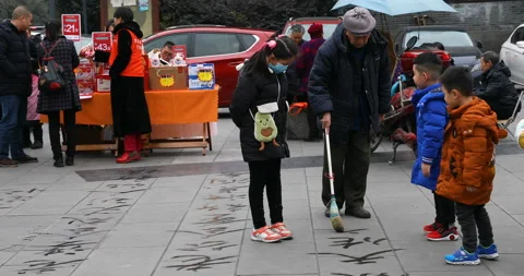 Old man practicing Chinese calligraphy with big bruch and water on the floor Stock Footage 124444248