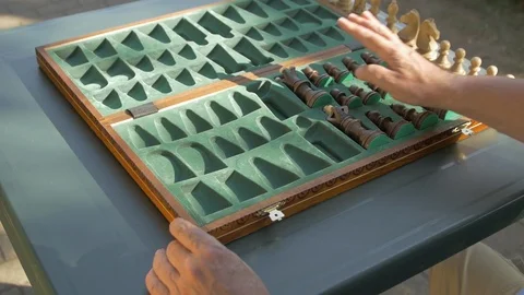 Old man prepares the chess game outside in the garden at the table and puts the Stock Footage 118605536