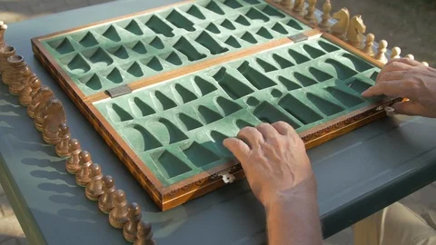 Old man prepares the chess game outside in the garden at the table and puts the Stock Footage 118606261