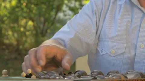 Old man prepares the chess game outside in the garden at the table and puts the Stock Footage 118710056