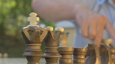 Old man prepares the chess game outside in the garden at the table and puts the Stock Footage 118721654