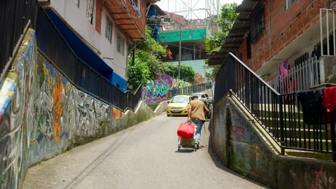 Old Man pushes Loaded Trolley Uphill along Narrow Graffiti Street Stock Footage 344365206