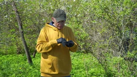 Old man puts black disposable mask on among green trees Stock Footage 130549773